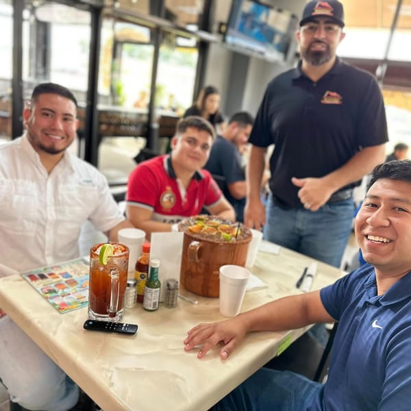 Four men smiling at a restaurant table with drinks and a large seafood dish.