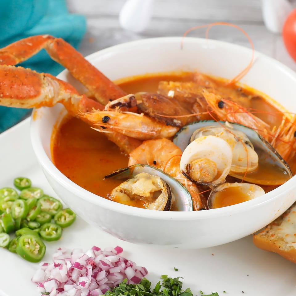 Seafood soup with crab legs, shrimp, mussels, and clams, served with garlic bread and garnishes.