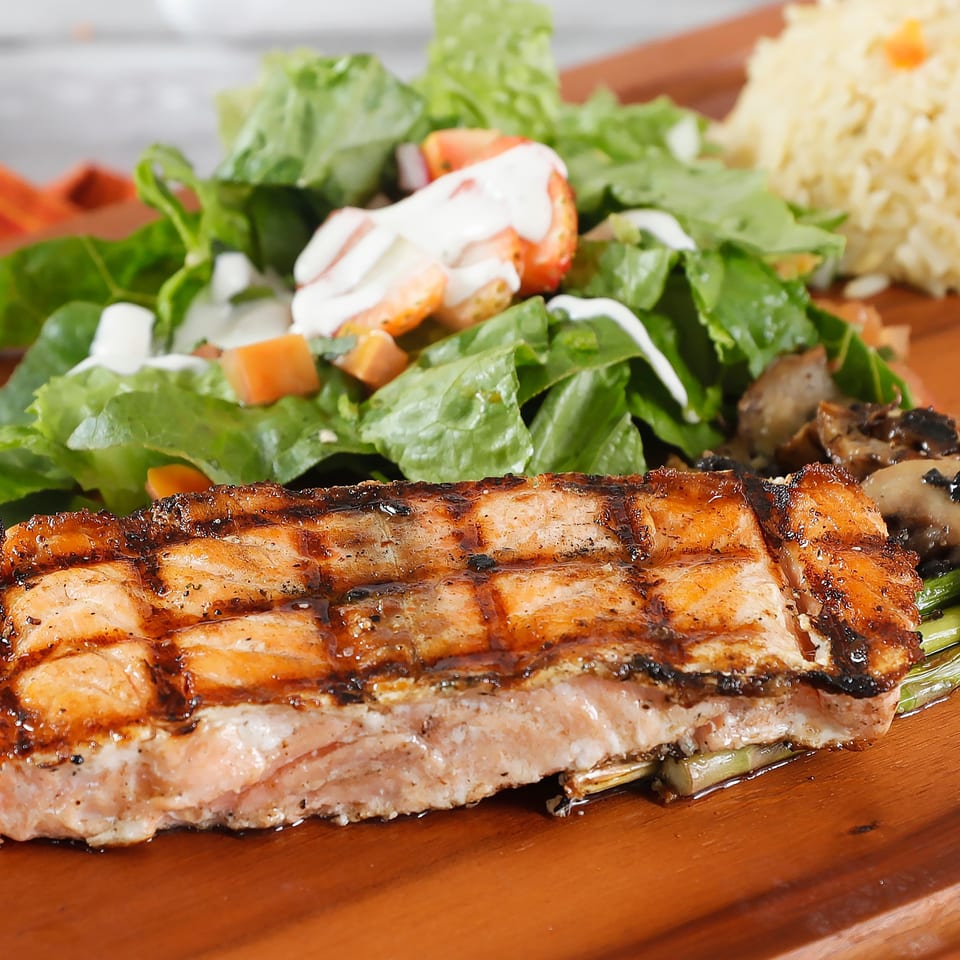 Grilled salmon with asparagus, mushrooms, a side salad, and rice on a wooden board.