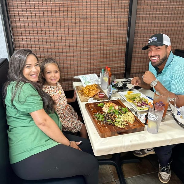 A family of three smiling at the camera while enjoying their meal at a restaurant.
