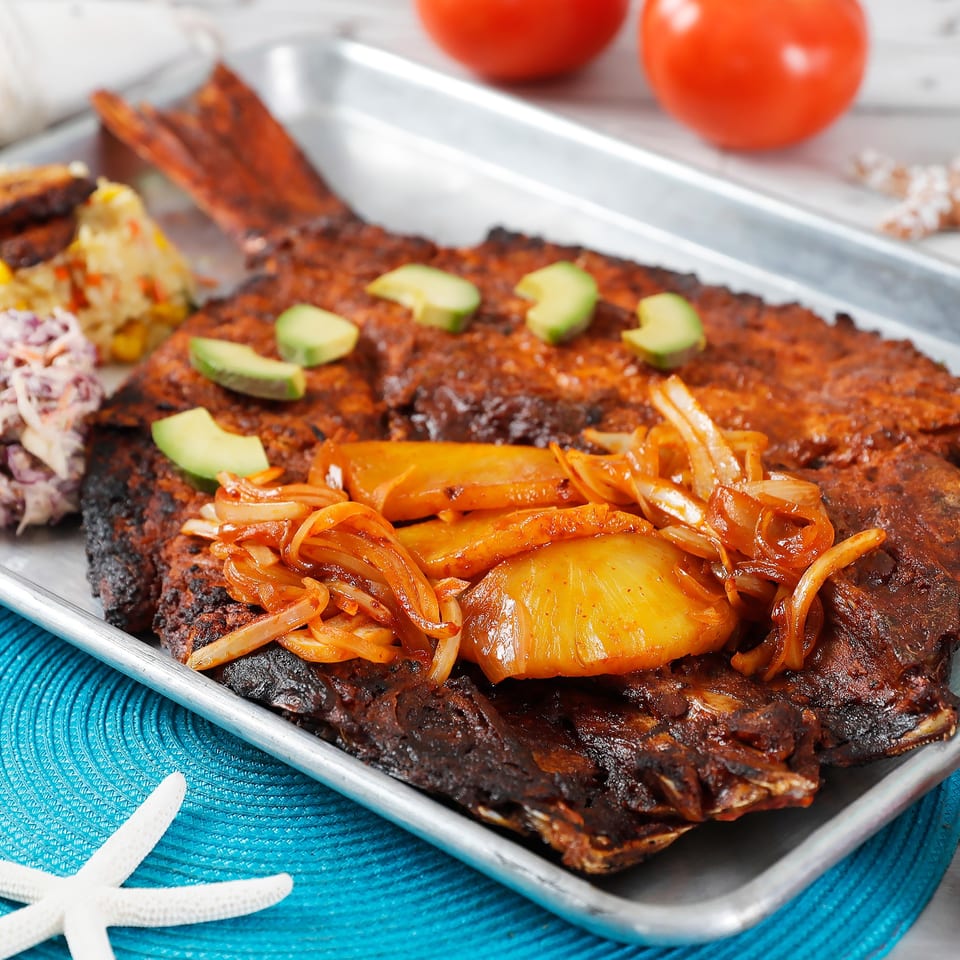 Whole grilled fish topped with onions and avocado, served with coleslaw and salad.